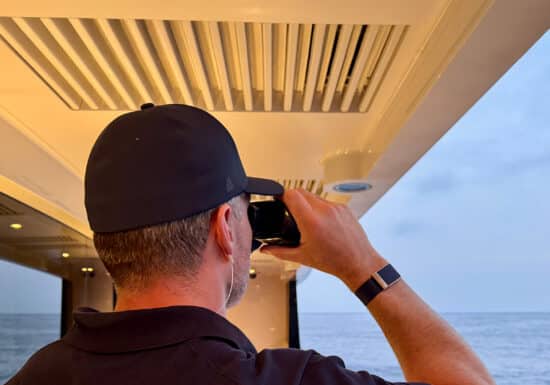 Superyacht Security | Man in a cap using binoculars from a yacht while looking out to sea.
