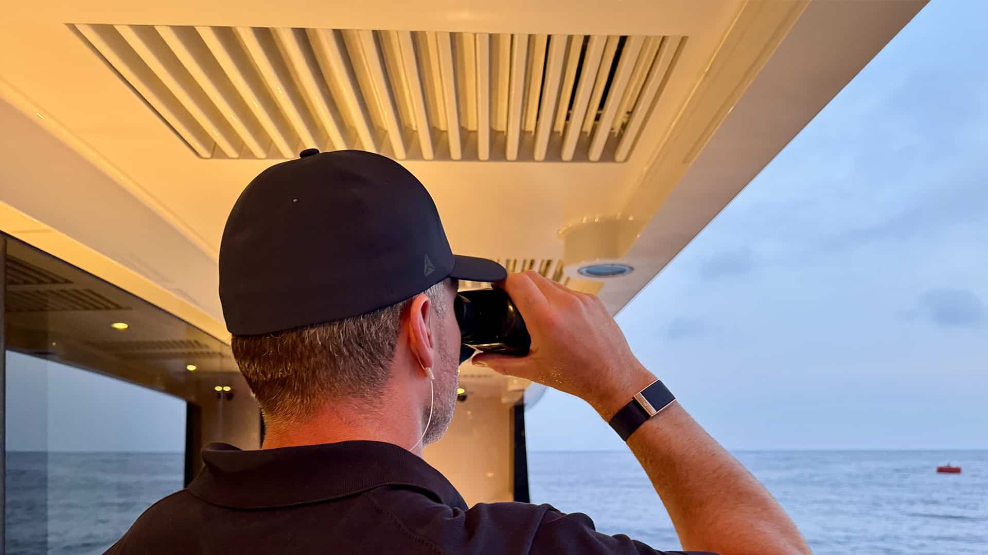 Superyacht Security | Man in a cap using binoculars from a yacht while looking out to sea.