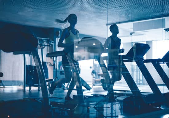 Bodyguard Jobs. Silhouettes of people running on treadmills in a modern gym, seen through a glass window.