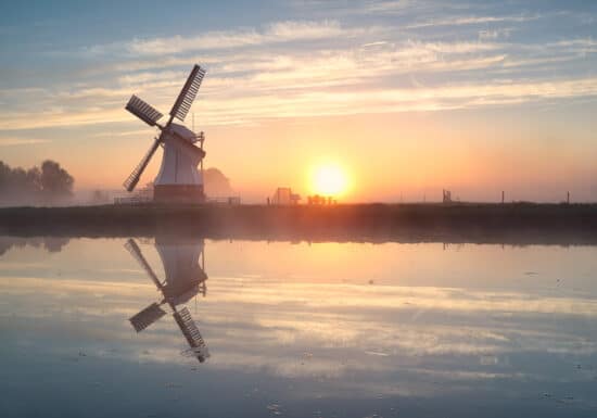 Is The Netherlands Safe?. A traditional windmill reflected in calm water during a misty sunrise.