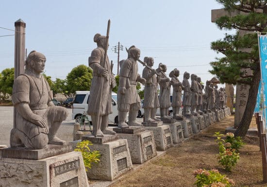 The History of Bodyguards and Intelligence. A row of samurai statues, each in different poses, standing in a park setting.