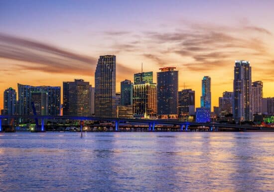 Bodyguard services in Miami. A skyline of Miami at sunset with illuminated skyscrapers and their reflections on the water.