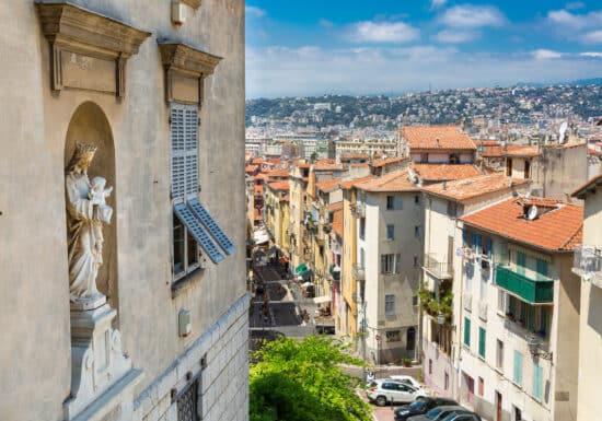 Bodyguard services in Nice. A view of rooftops and narrow streets in Nice, France, with a statue of the Virgin Mary on a building facade in the foreground.