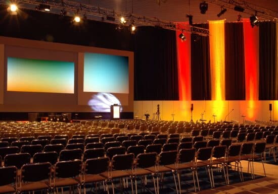 Corporate event security. An empty corporate event venue with rows of chairs, large screens, and colorful lighting.