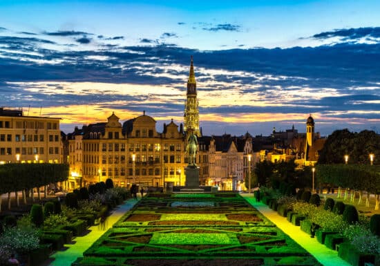 Bodyguard services in Belgium. The cityscape of Brussels at dusk, highlighting a well-lit garden and historic buildings under a colorful sky.