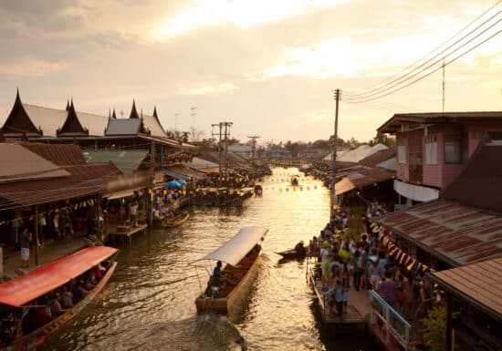 Bodyguard Services in Thailand. Busy floating market in Thailand with traditional boats and houses along the canal during sunset.