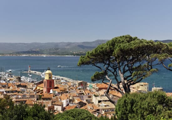 Cote d'Azur Bodyguard Services. Scenic view of Saint-Tropez, France, with red-roofed buildings and a marina set against the backdrop of mountains and sea.