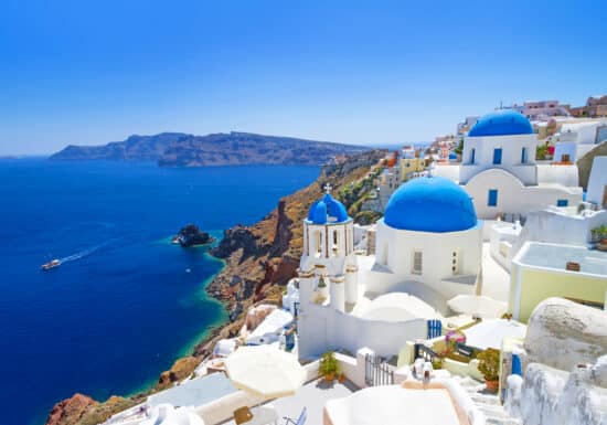 Bodyguard Services on Mykonos. Iconic blue-domed churches and white buildings of Santorini overlooking the deep blue Aegean Sea.