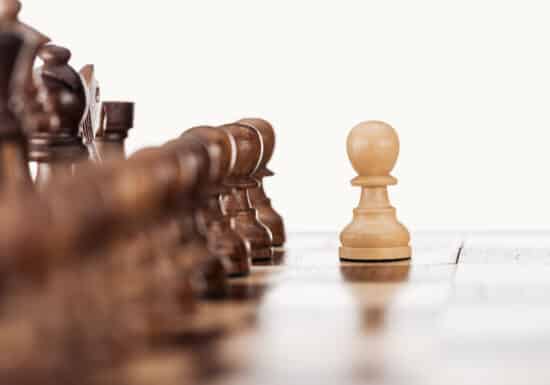 International Executive Protection Company. Close-up of a white pawn standing in front of brown chess pieces on a chessboard.