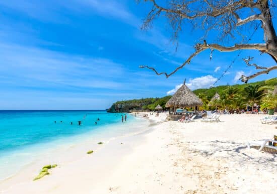 Bodyguard services in Curaçao. A tropical beach with clear blue water and thatched umbrellas.