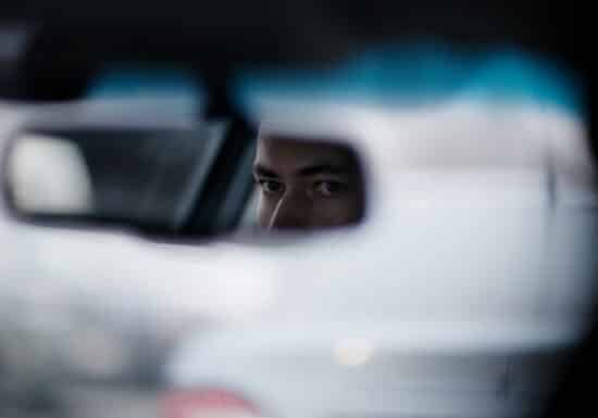 Security driver. A man’s eyes are visible in the rearview mirror of a car, with the background blurred.