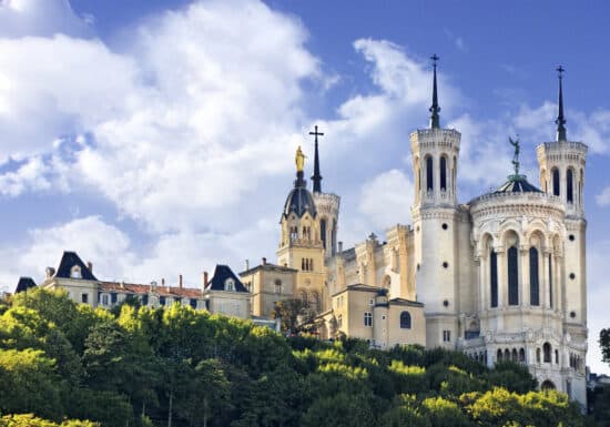 Body guard services in France. The Basilica of Notre-Dame de Fourvière in Lyon, France, standing atop a green hill under a blue sky.