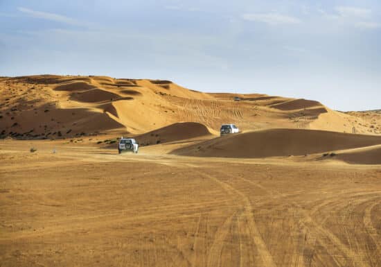 Hostile Environment Close Protection. Two off-road vehicles driving on sand dunes in a desert, leaving tracks behind.