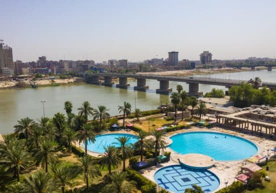 Private Security Services in Iraq. Aerial view of a city with a river, bridge, palm trees, and blue pools.