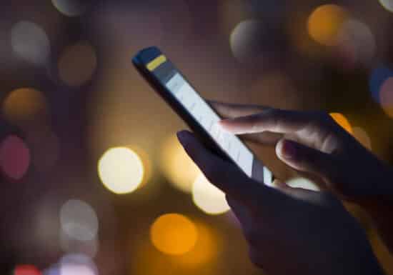 Bodyguards near me. Close-up of hands using a smartphone with a glowing screen at night.