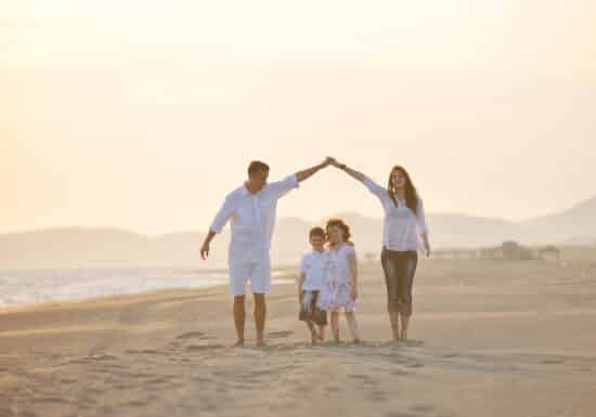 Family Security Management. Family of four holding hands and walking on a sandy beach at sunset.