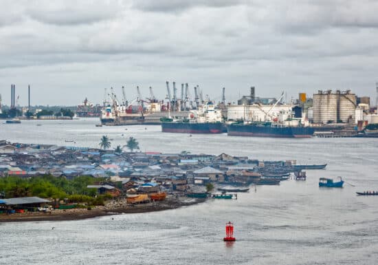 Maritime Security in West Africa. Industrial port with ships and cranes, with a local settlement in the foreground.