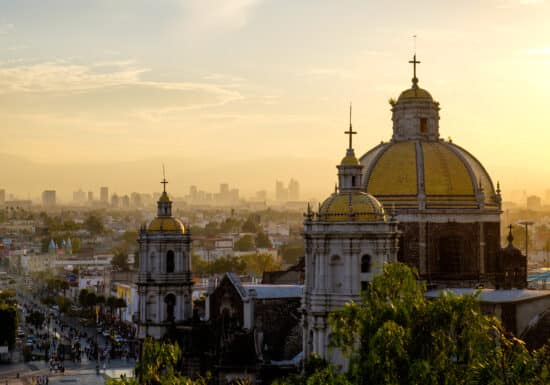 Bodyguard services in Mexico. A view of the Mexico City skyline at sunset with prominent church domes in the foreground.