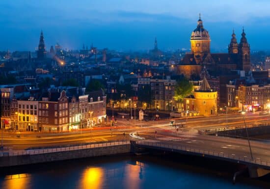 Hire a Bodyguard in Amsterdam. A night view of Amsterdam's illuminated cityscape with prominent historical buildings and bridges.