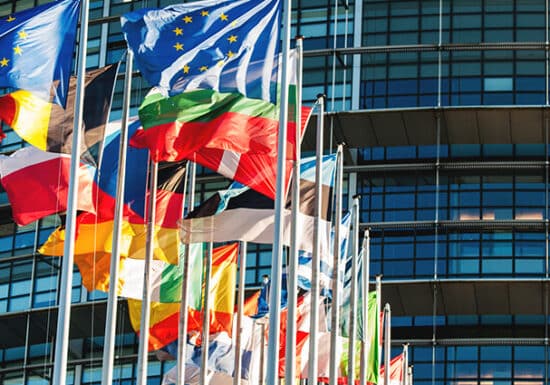 Geopolitical Risk Analysis. A row of international flags flying outside a modern glass building.