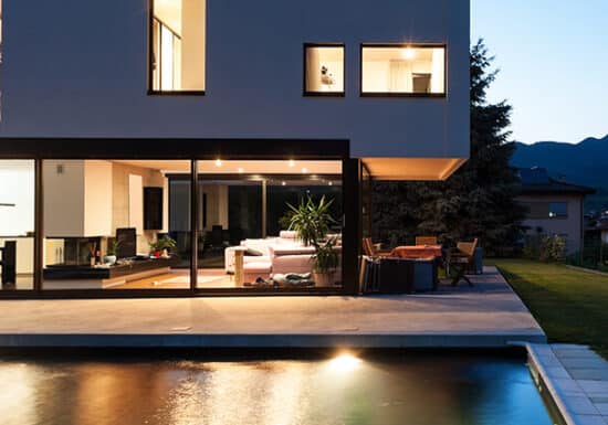 Residential Security Services. A modern house with large glass windows, a pool, and a view of the mountains at dusk.