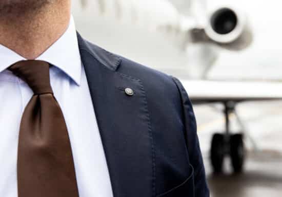 Global Security Company. Close-up of a person wearing a dark blue suit with a white shirt and brown tie, featuring a small lapel pin.