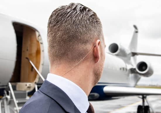 Bodyguard for Hire. Bodyguard with an earpiece, standing by a private jet."