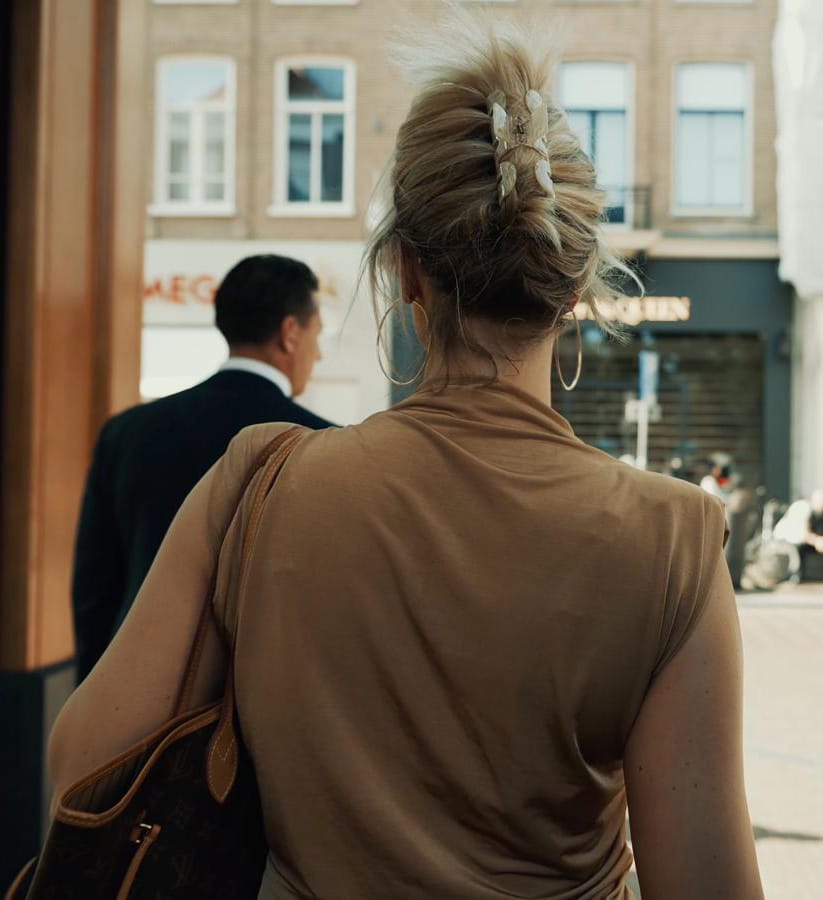 Woman with handbag walking out onto a city street accompanied by a man in suit.